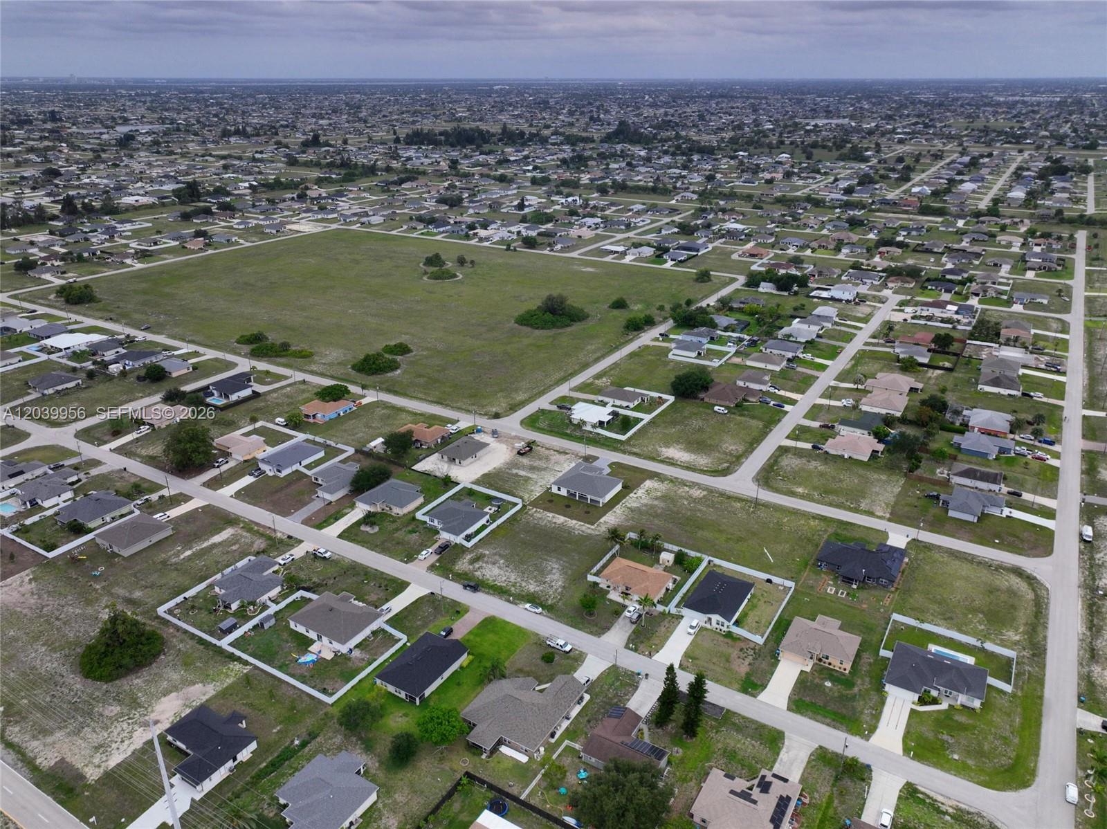 An aerial view shows a suburban neighborhood with scattered houses and a large vacant field — 530 NW 23RD TER, Cape Coral FL 33993, CAPE CORAL, FL