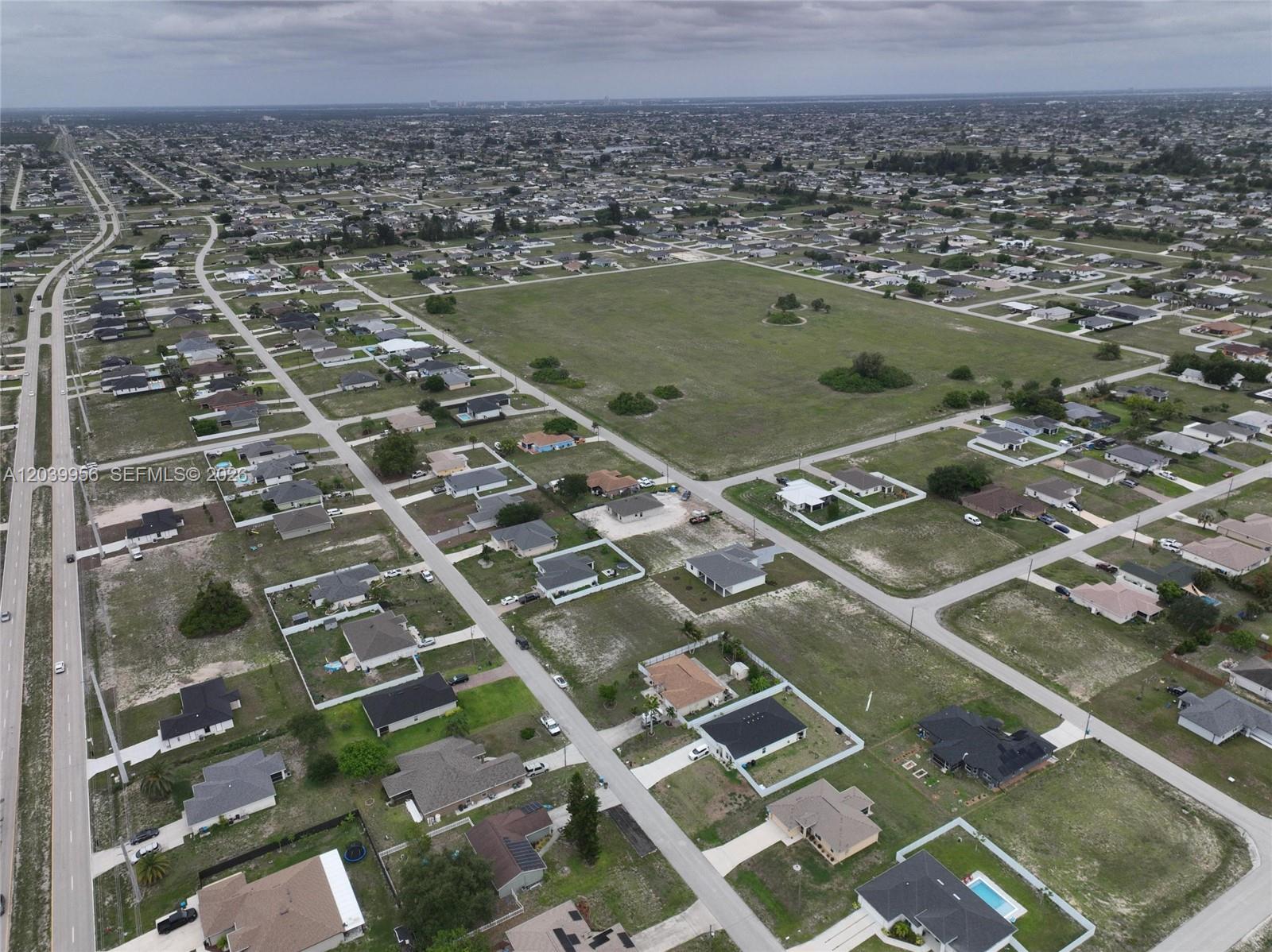 An aerial view shows a suburban neighborhood with scattered houses and large vacant grassy lots — 530 NW 23RD TER, Cape Coral FL 33993, CAPE CORAL, FL