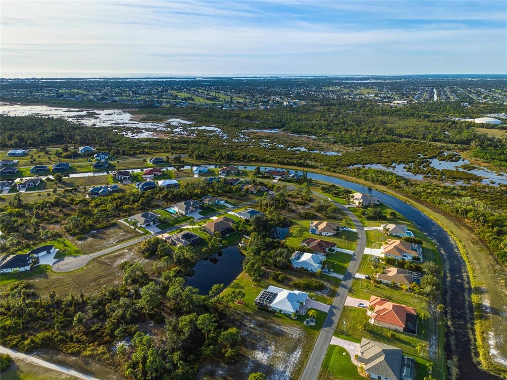 An aerial view shows a suburban neighborhood with houses, a small pond, and surrounding wetlands — 14 PINE VALLEY ROAD, ROTONDA WEST, FL
