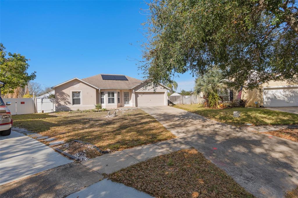 A single-story suburban house with a concrete driveway, a two-car garage, and solar panels — 327 RIDGE COURT, APOPKA, FL