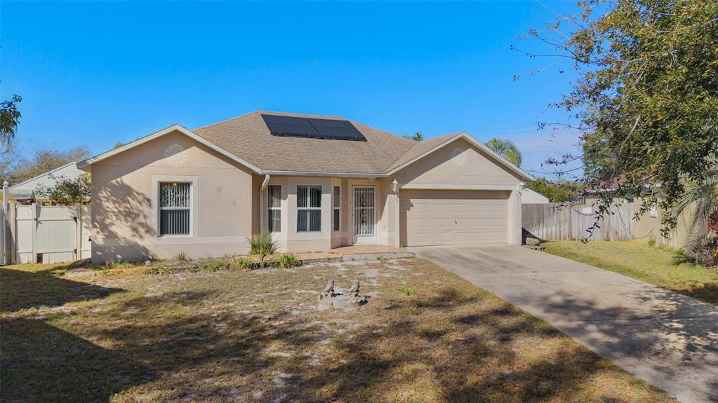 A single-story suburban house with a tan stucco exterior, a two-car garage, and solar panels — 327 RIDGE COURT, APOPKA, FL