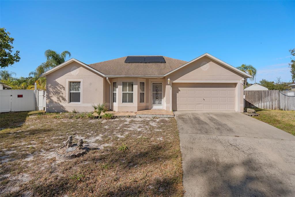 A single-story beige house with a concrete driveway, solar panels, and a front yard — 327 RIDGE COURT, APOPKA, FL