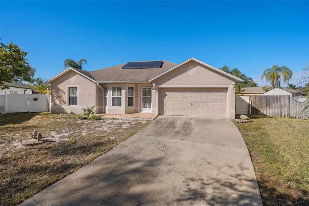 A single-story house with a beige stucco exterior, a concrete driveway, and roof solar panels — 327 RIDGE COURT, APOPKA, FL