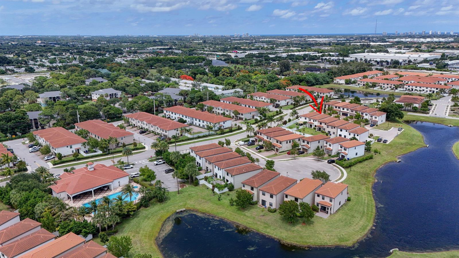 An aerial view shows a residential community with townhomes, a swimming pool, and a lake — 4009 Sequoia Place, Riviera Beach FL 33410, RIVIERA BEACH, FL