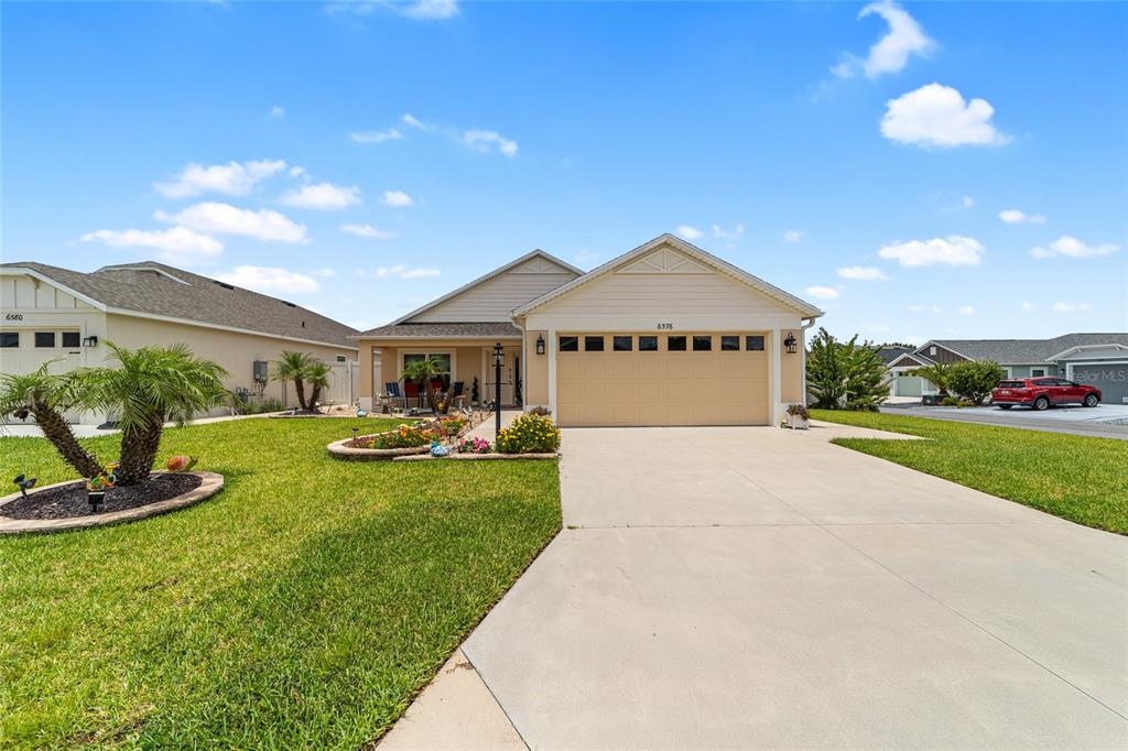 A single-story house with a beige exterior, a two-car garage, and a manicured front lawn — 6576 MERRILL LANE, THE VILLAGES, FL