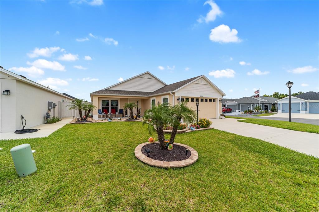 A single-story suburban house with a tan garage, beige siding, and a landscaped front yard — 6576 MERRILL LANE, THE VILLAGES, FL