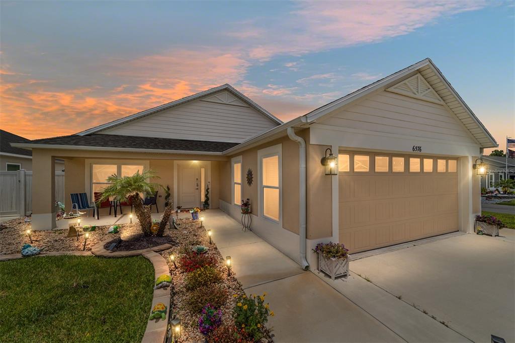 A single-story house with a tan exterior, a two-car garage, and a landscaped front yard — 6576 MERRILL LANE, THE VILLAGES, FL