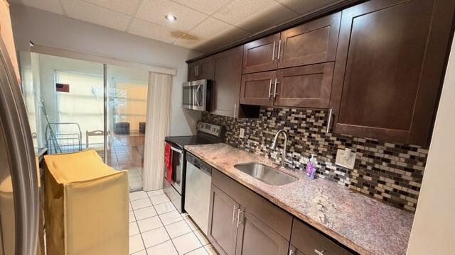 A kitchen features dark wood cabinets, granite countertops, a mosaic backsplash, and stainless steel appliances — 5 Abbey Lane # 104, Delray Beach FL 33446, DELRAY BEACH, FL