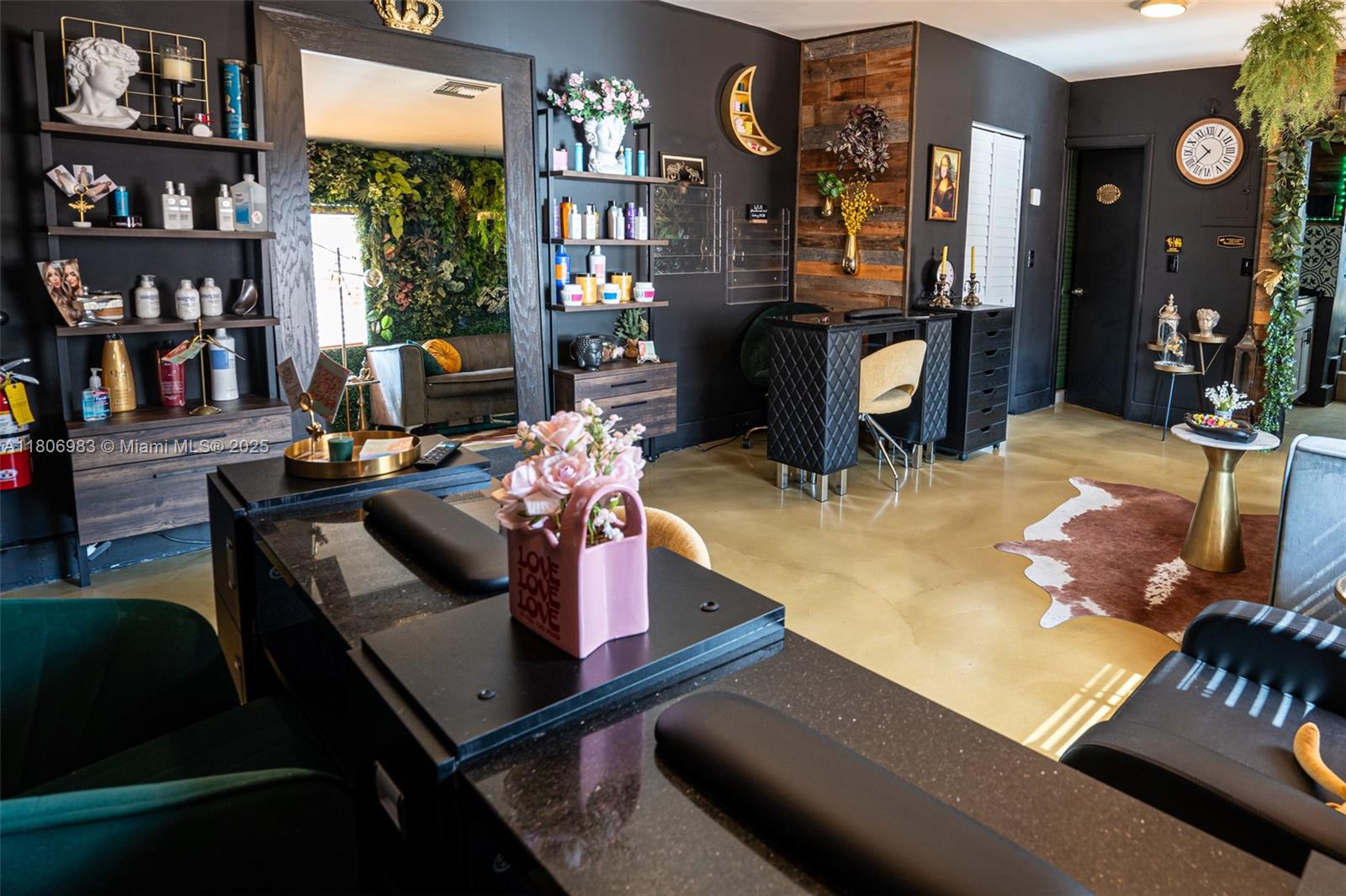 A modern salon interior features dark walls, black workstations, wood accents, and decorative greenery — 3436 N Miami Ave, Miami FL 33127, MIAMI, FL