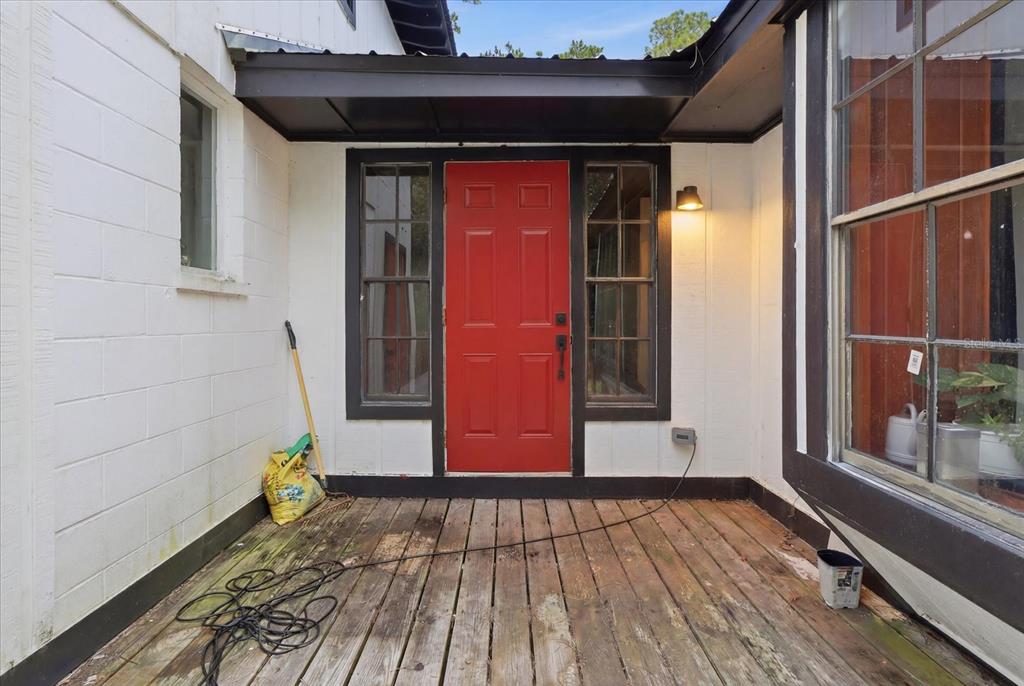 A wooden deck leads to a red front door flanked by windows under a roof overhang — 1019 S MILDRED AVENUE, BROOKSVILLE, FL