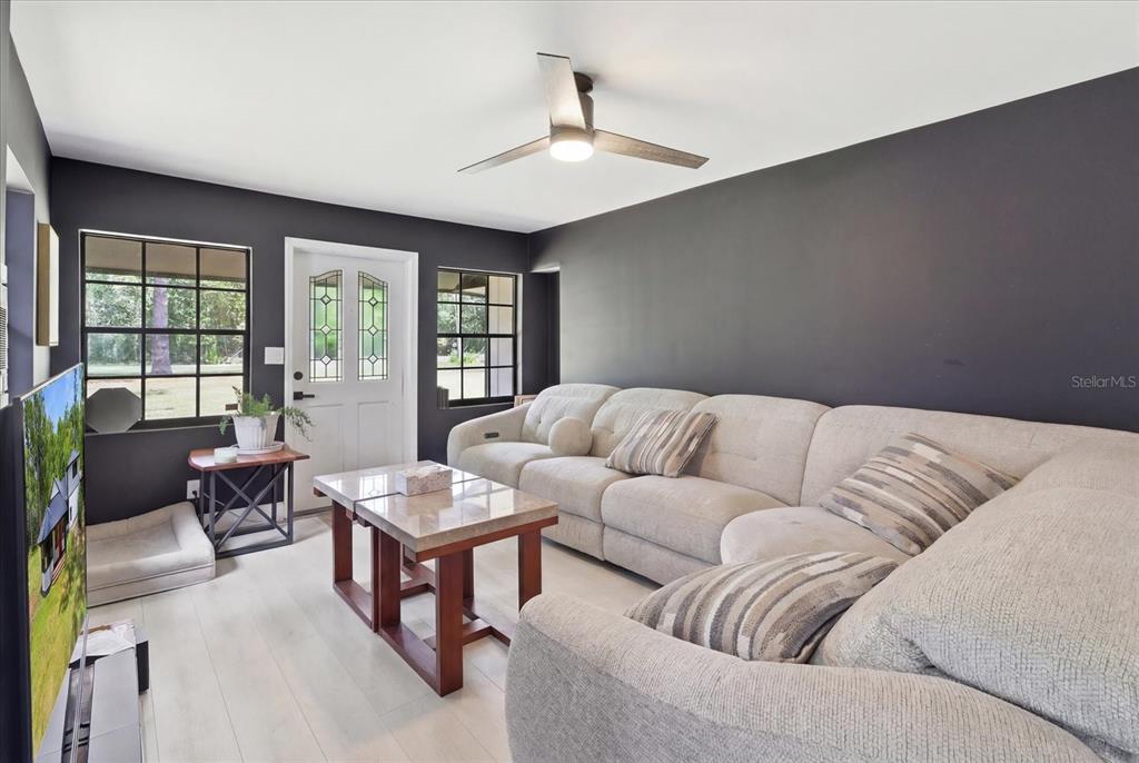 A living room features dark gray walls, light wood flooring, a sectional sofa, and windows — 1019 S MILDRED AVENUE, BROOKSVILLE, FL