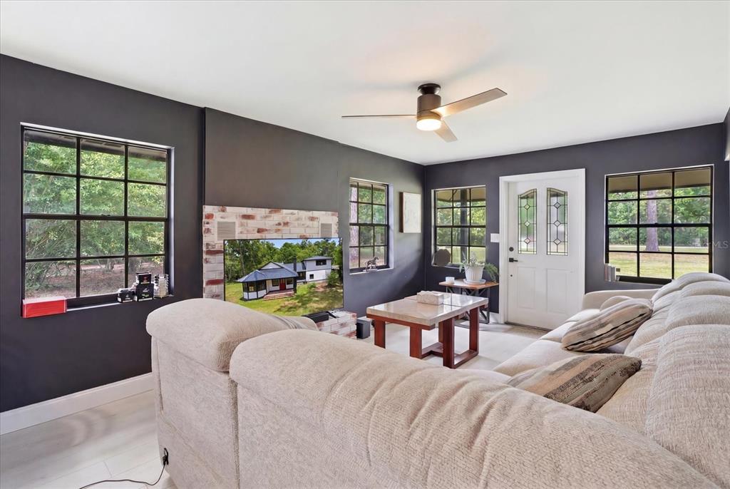 A living room features dark gray walls, a brick fireplace, a ceiling fan, and windows — 1019 S MILDRED AVENUE, BROOKSVILLE, FL