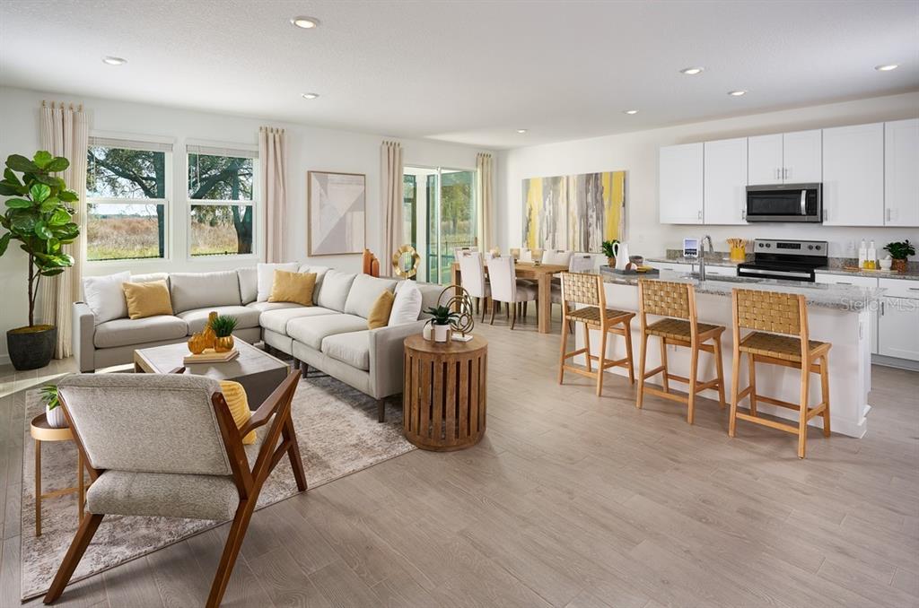 An open-concept living room and kitchen featuring light wood floors and white cabinetry — 83 WANDERING CREEK WAY, PALM COAST, FL