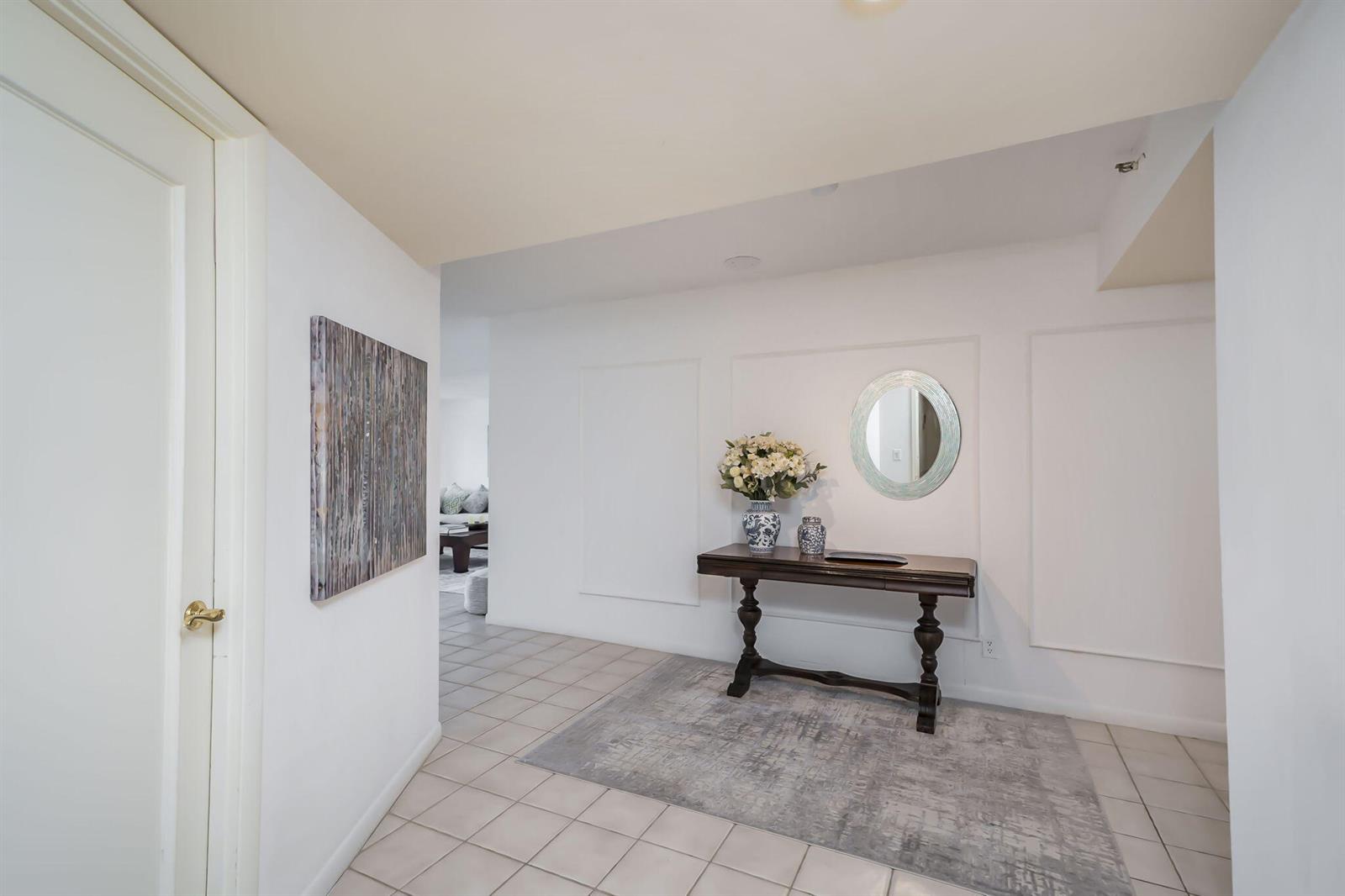 A tiled entryway features a console table, a round mirror, and wall molding — 4301 N Ocean Boulevard # A206, Boca Raton FL 33431, BOCA RATON, FL