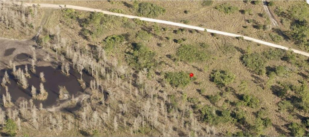 An aerial view shows a dirt road, a small pond, and a red marker on land — HOLOPAW GROVES ROAD, ST CLOUD, FL