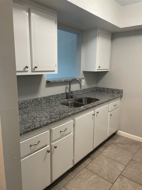 A kitchen features white cabinets, granite countertops, a double sink, and gray tile flooring — 675 INDIAN ROCKS ROAD N UNIT 209D, BELLEAIR BLUFFS, FL