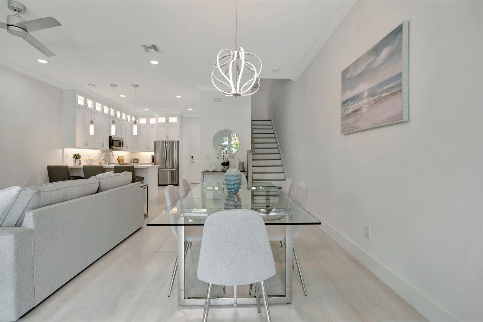 A modern open-concept dining area features a glass table, upholstered chairs, and a contemporary chandelier — 4695 SE Manatee Way, Stuart FL 34997, STUART, FL