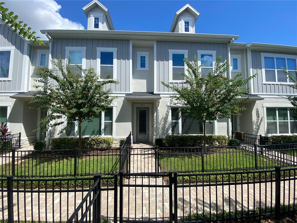 A two-story townhouse exterior features gray vertical siding, a front gate, and two dormer windows — 1011 LYCHEE COURT, LAKE MARY, FL