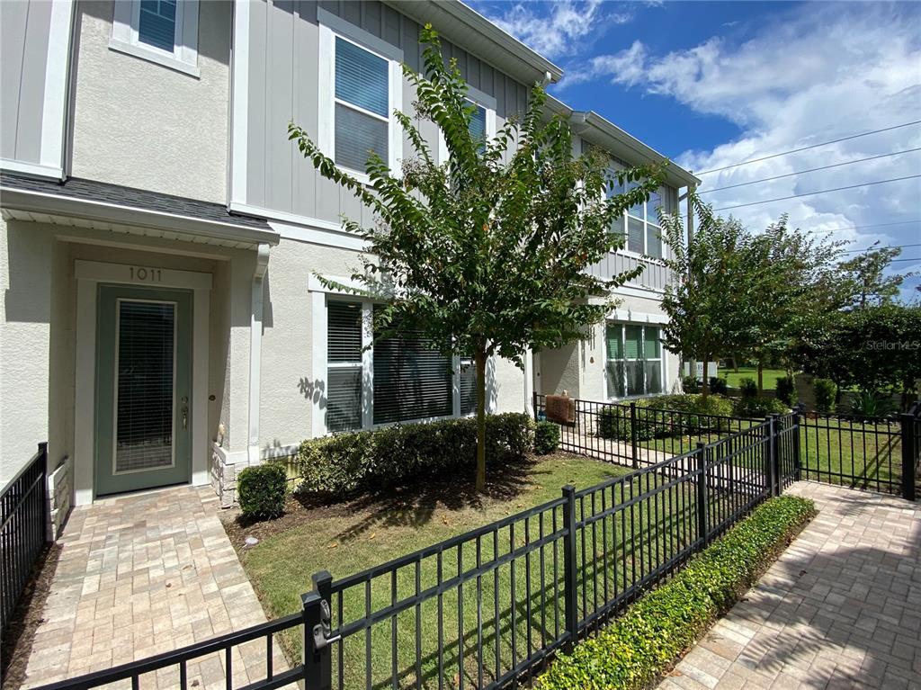 A two-story townhouse exterior features a light green front door, paved walkway, and metal fencing — 1011 LYCHEE COURT, LAKE MARY, FL