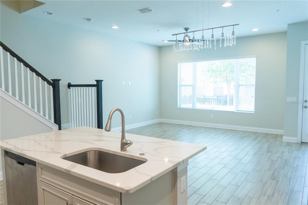 A kitchen island with a sink and quartz countertop overlooks a living area with stairs — 1011 LYCHEE COURT, LAKE MARY, FL