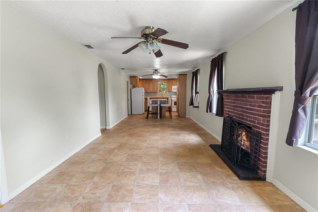 A living room with tile flooring and a brick fireplace leads to an open kitchen — 30 E 8TH STREET, FROSTPROOF, FL