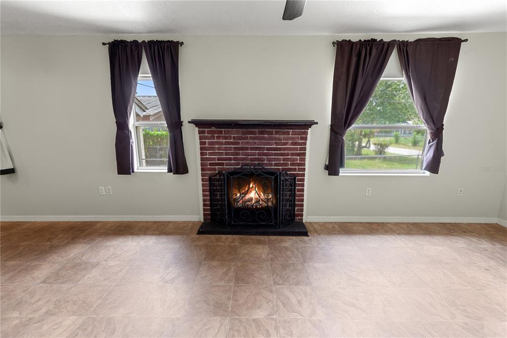 A living room features a brick fireplace, tile flooring, and two windows with dark curtains — 30 E 8TH STREET, FROSTPROOF, FL