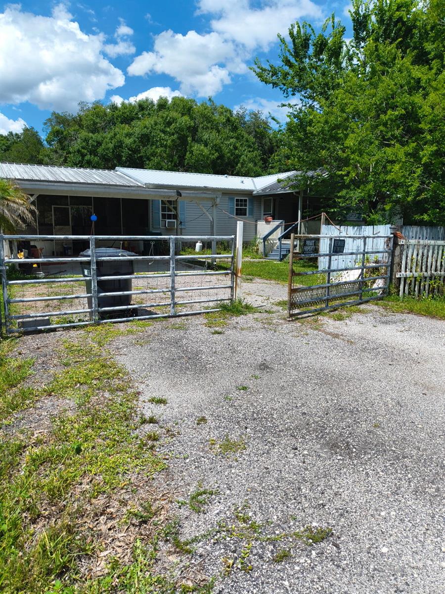 A gravel driveway leads to a single-story house with a carport and metal gate — 6725 NE 8th Lane, Okeechobee FL 34974, OKEECHOBEE, FL