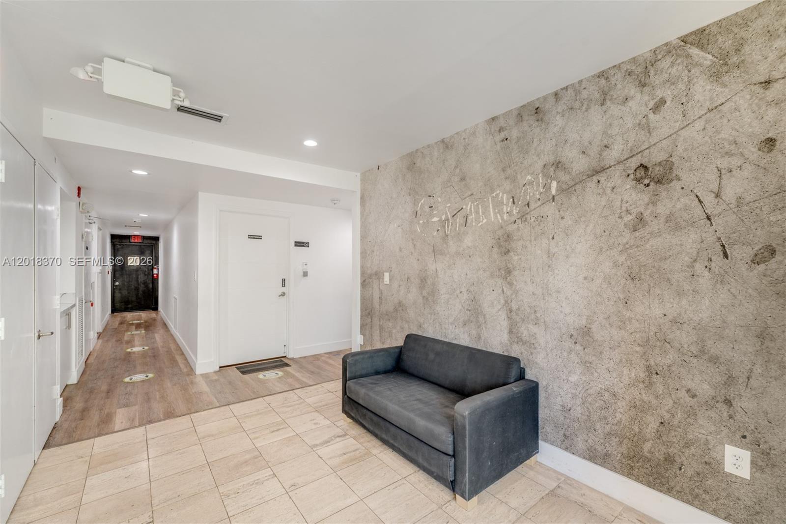 A grey sofa sits against a textured concrete wall in a tiled building hallway — 1378 SW 22nd St # 2, Miami FL 33145, MIAMI, FL