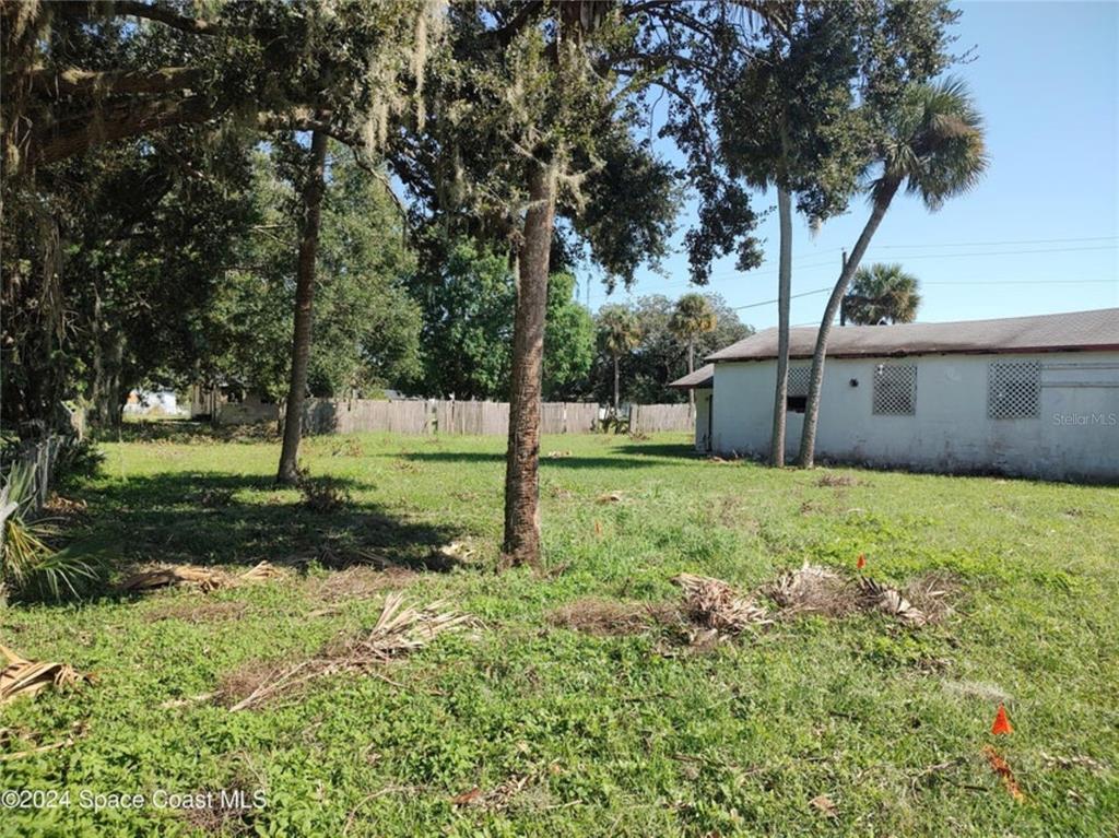 A grassy backyard features several mature trees and a white building with lattice-covered windows — 929 S DELEON AVENUE, TITUSVILLE, FL