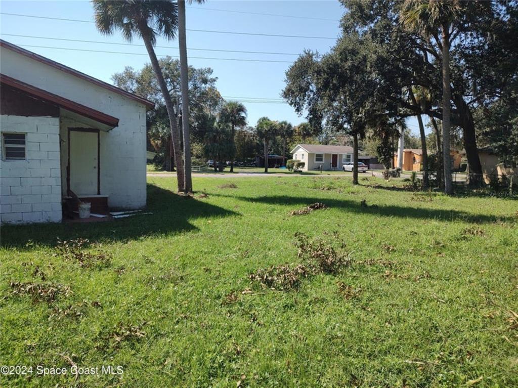 A grassy yard sits beside a white concrete block house with palm trees — 929 S DELEON AVENUE, TITUSVILLE, FL