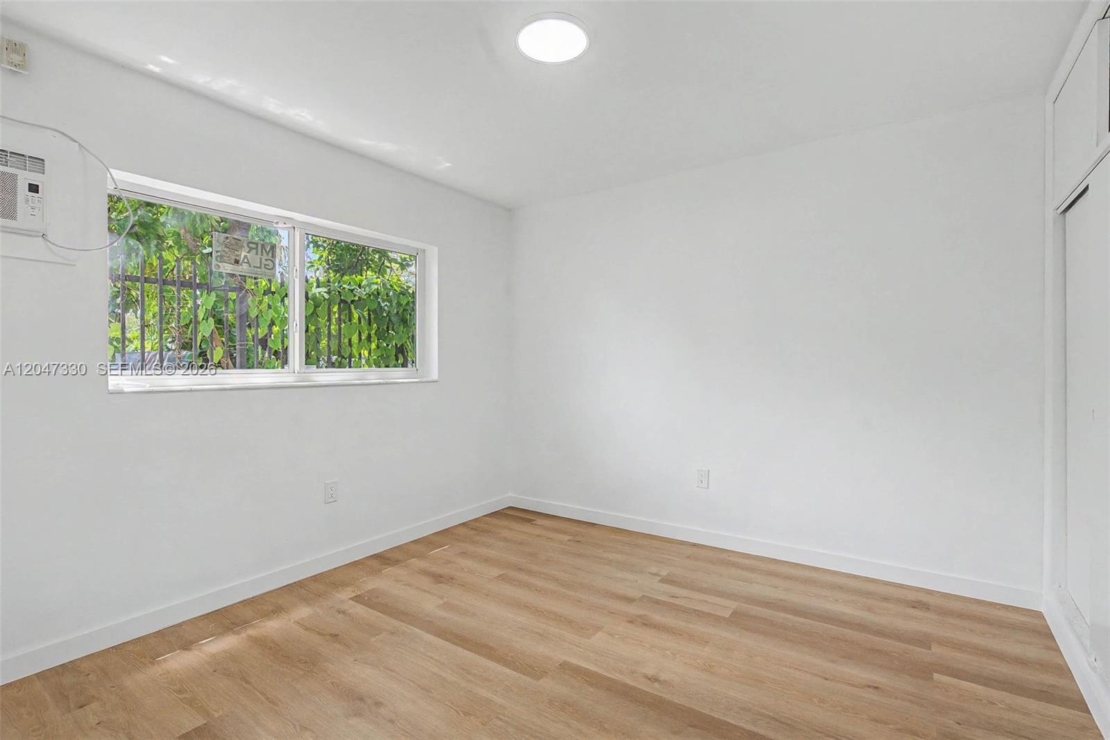 An empty bedroom features white walls, light wood-look flooring, a window, and a ceiling light — 60 NW 79th St # 27, Miami FL 33150, MIAMI, FL