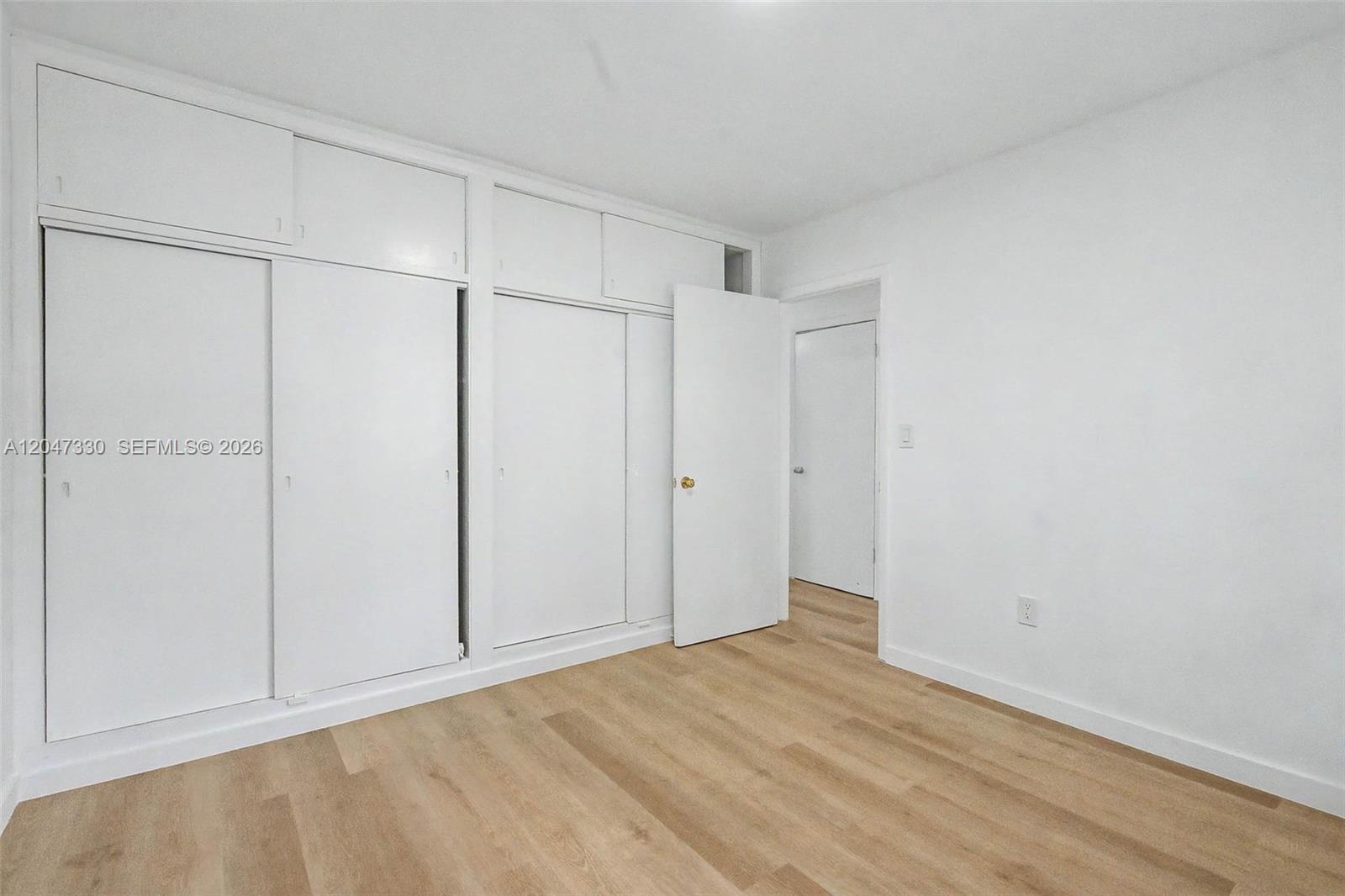 A bedroom features white walls, light wood-look flooring, and built-in white storage closets — 60 NW 79th St # 27, Miami FL 33150, MIAMI, FL