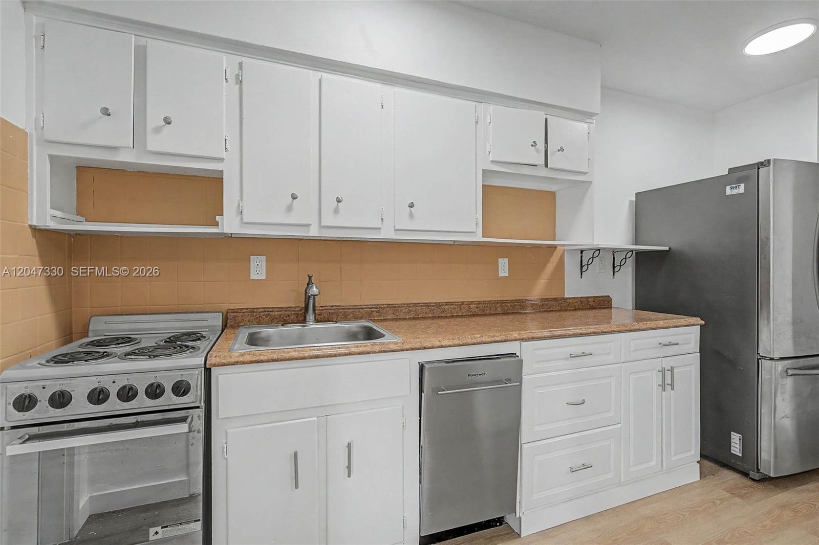 A kitchen features white cabinets, a stainless steel dishwasher, a stove, and tan tile backsplash — 60 NW 79th St # 27, Miami FL 33150, MIAMI, FL