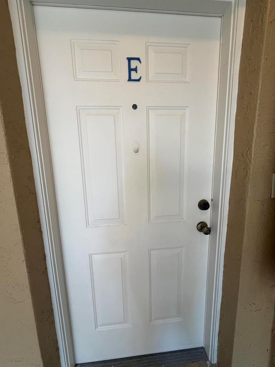 A white exterior door labeled with the letter E features a peephole and two locks — 154 Village Boulevard, Tequesta FL 33469, TEQUESTA, FL