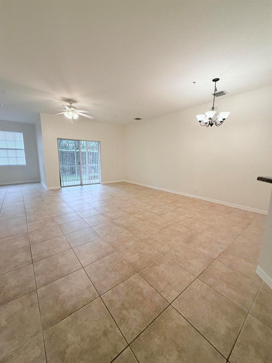 An empty living area features beige tile flooring, a ceiling fan, and sliding glass doors — 154 Village Boulevard, Tequesta FL 33469, TEQUESTA, FL