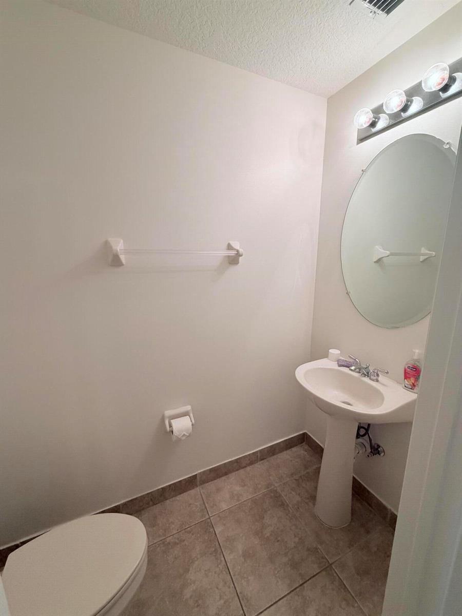 A small bathroom features a pedestal sink, an oval mirror, and a towel bar — 154 Village Boulevard, Tequesta FL 33469, TEQUESTA, FL