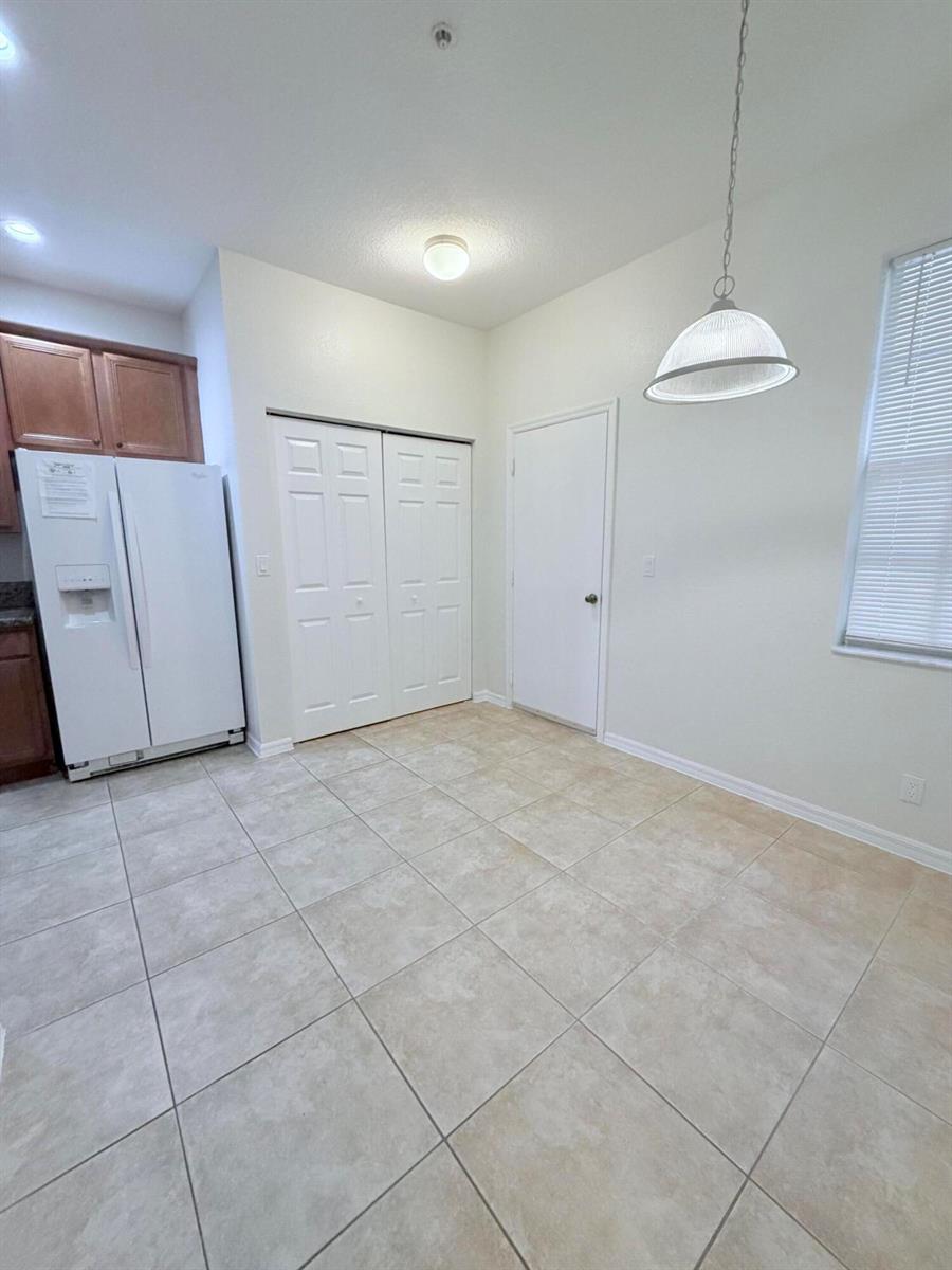 A kitchen dining area features tile flooring, a white refrigerator, and a pendant light — 154 Village Boulevard, Tequesta FL 33469, TEQUESTA, FL