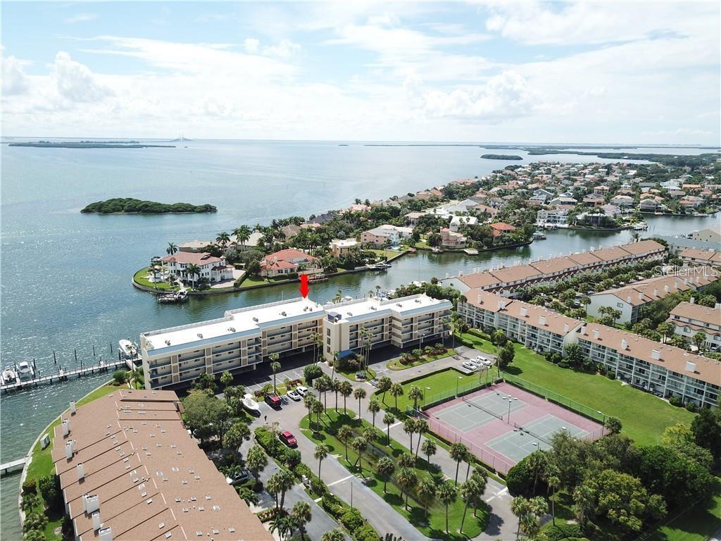 An aerial view shows a multi-story waterfront condominium complex with a tennis court and docks — 363 PINELLAS BAYWAY S UNIT 36, TIERRA VERDE, FL