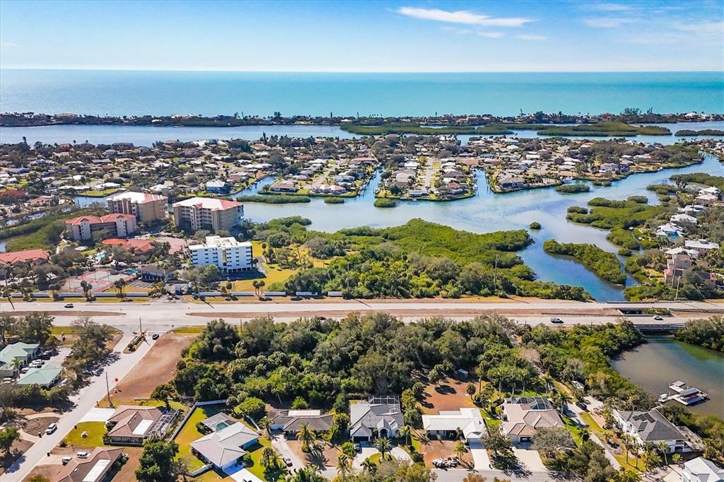 An aerial view shows a coastal neighborhood with houses, mangroves, and a nearby ocean horizon — 2099 S TAMIAMI TRAIL, OSPREY, FL
