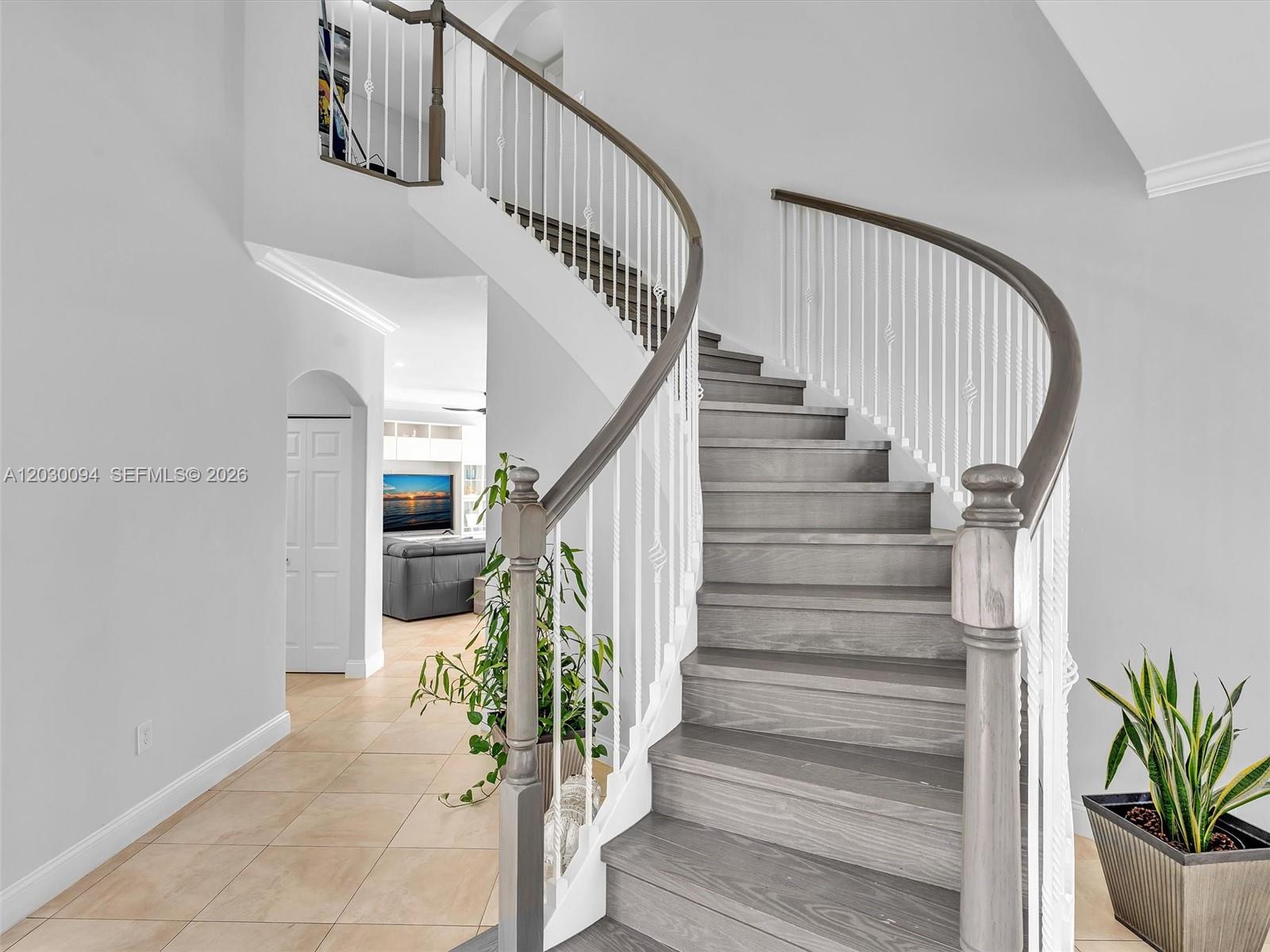 A curved staircase with wooden treads and white balusters sits in a tiled entryway — 4971 SW 158th Ave, Miramar FL 33027, MIRAMAR, FL