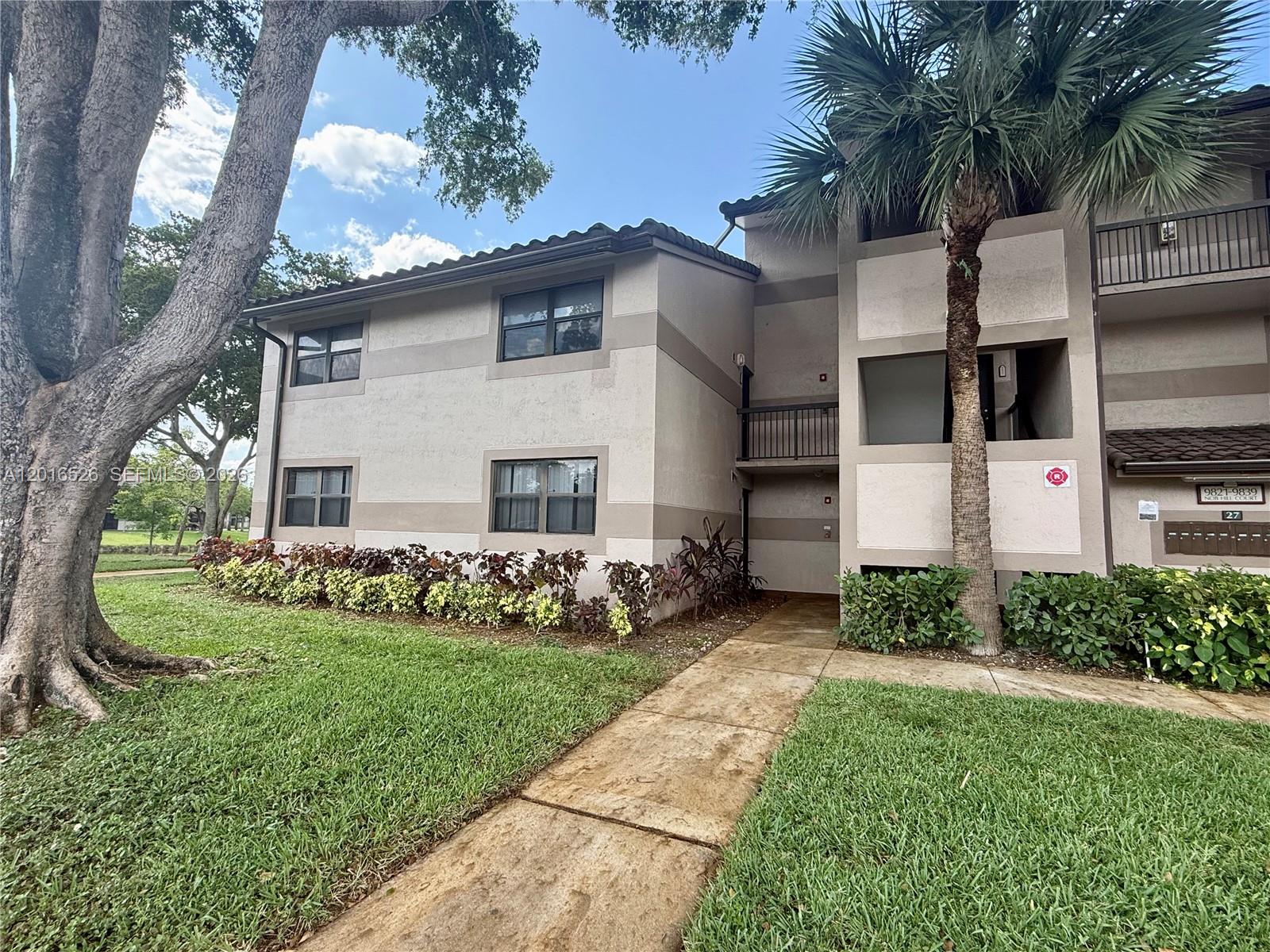 A two-story apartment building exterior features a concrete walkway, a palm tree, and landscaping — 9827 Nob Hill Ct # 0, Sunrise FL 33351, SUNRISE, FL