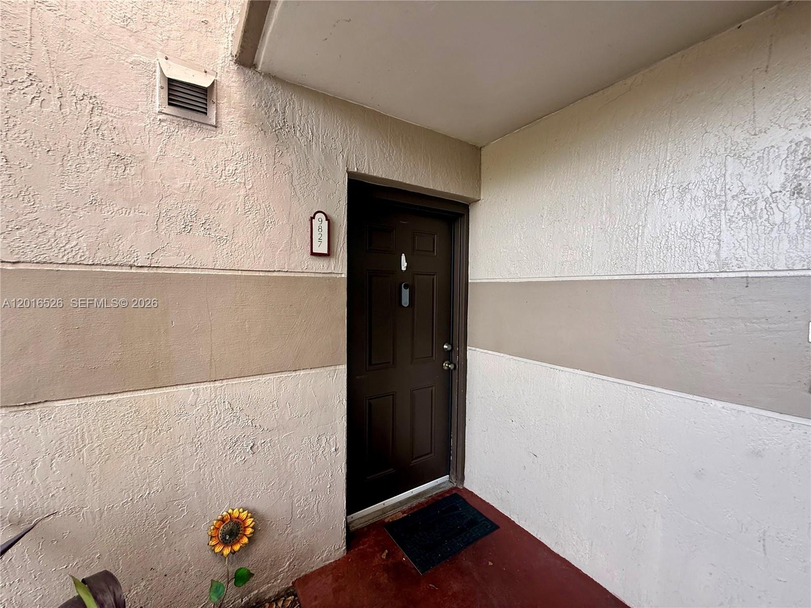 A dark brown front door with a smart lock is set into a stucco wall — 9827 Nob Hill Ct # 0, Sunrise FL 33351, SUNRISE, FL