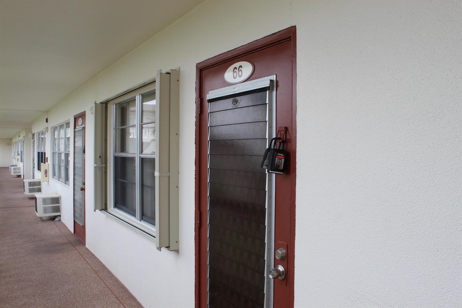 An exterior view of a motel-style building with numbered doors and windows along a walkway — 66 Brighton, Boca Raton FL 33434, BOCA RATON, FL