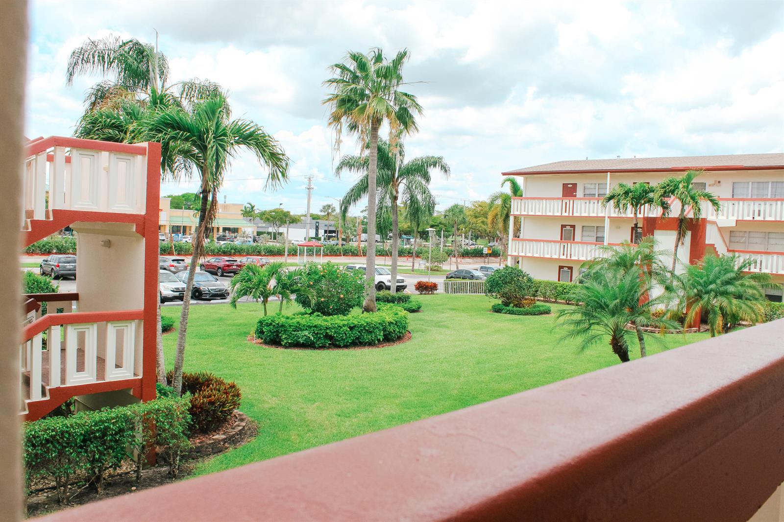 A view from a balcony overlooking a grassy courtyard with palm trees and apartment buildings — 66 Brighton, Boca Raton FL 33434, BOCA RATON, FL