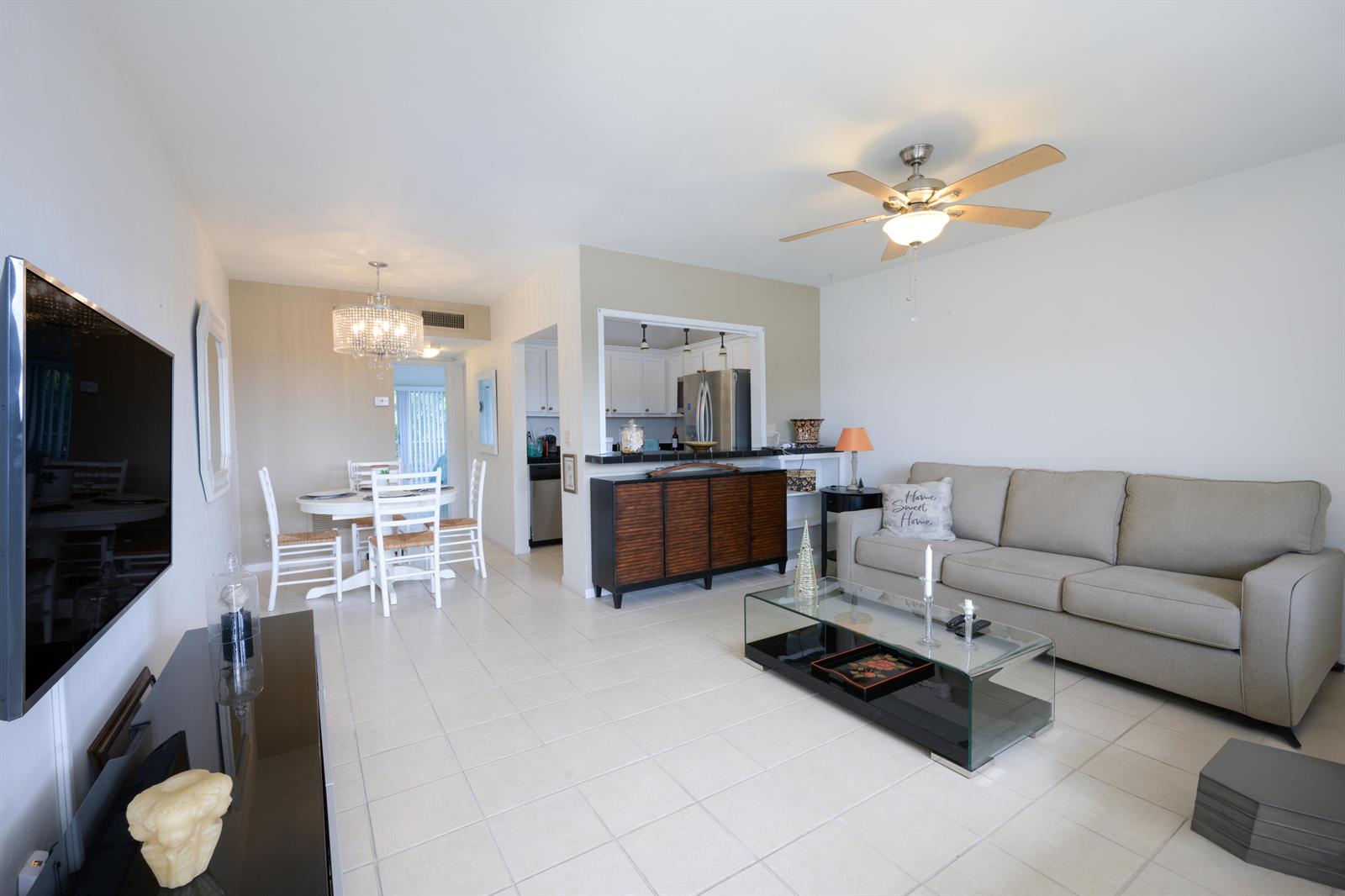 A living room with tile floors, a beige sofa, and an open kitchen pass-through window — 3402 Cynthia Lane # 208, FL 33461, FL