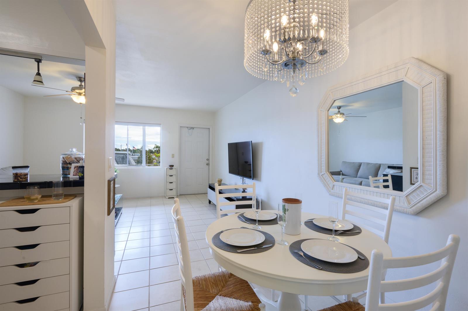 A dining area with a round white table, chandelier, and large mirror on a white wall — 3402 Cynthia Lane # 208, FL 33461, FL