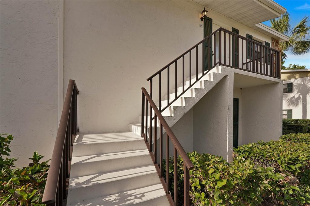 An exterior view of a white building with a concrete staircase leading to a balcony — 5400 34TH STREET W UNIT I9, BRADENTON, FL