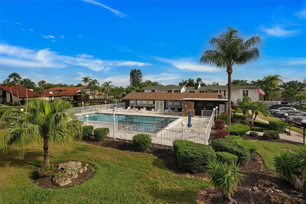 An outdoor swimming pool is enclosed by a white fence near a community building — 5400 34TH STREET W UNIT I9, BRADENTON, FL