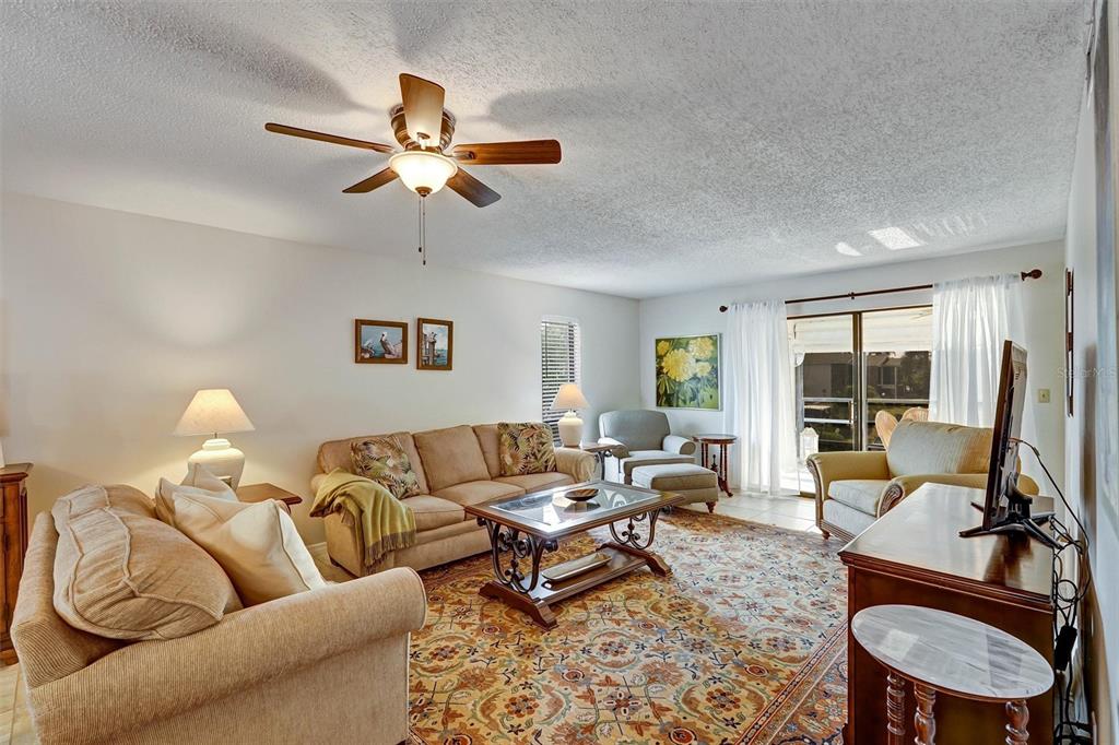 A living room features a patterned area rug, a ceiling fan, and sliding glass doors — 5400 34TH STREET W UNIT I9, BRADENTON, FL