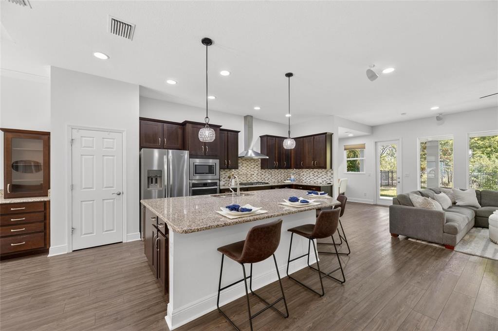 A kitchen with dark wood cabinets, granite countertops, and an island opens to a living area — 6411 BLUE SAIL LANE, APOLLO BEACH, FL